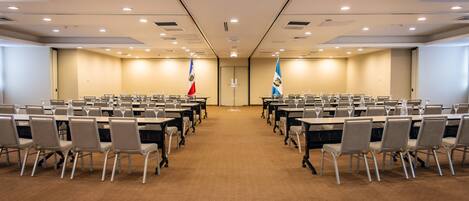 A conference room with rows of tables and chairs, flags, and a carpeted floor.