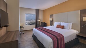 Une chambre d’hôtel avec un grand lit, un bureau avec une chaise, une télévision et une fenêtre donnant sur la ville.
