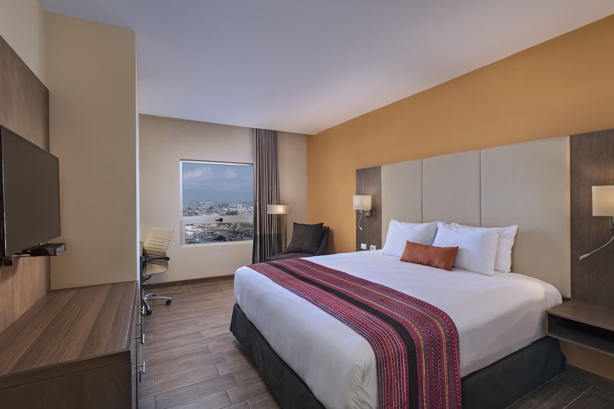 Una habitación de hotel con una cama grande, un escritorio con una silla, un televisor y una ventana con vistas a la ciudad.