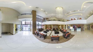 Un hall d’entrée spacieux avec un espace salon central, un plafond haut orné d’un lustre, et un balcon situé au deuxième étage.