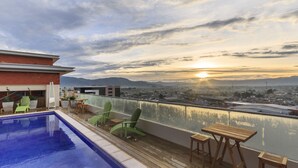 Une piscine sur le toit, offrant une vue sur la ville et les montagnes au coucher du soleil.