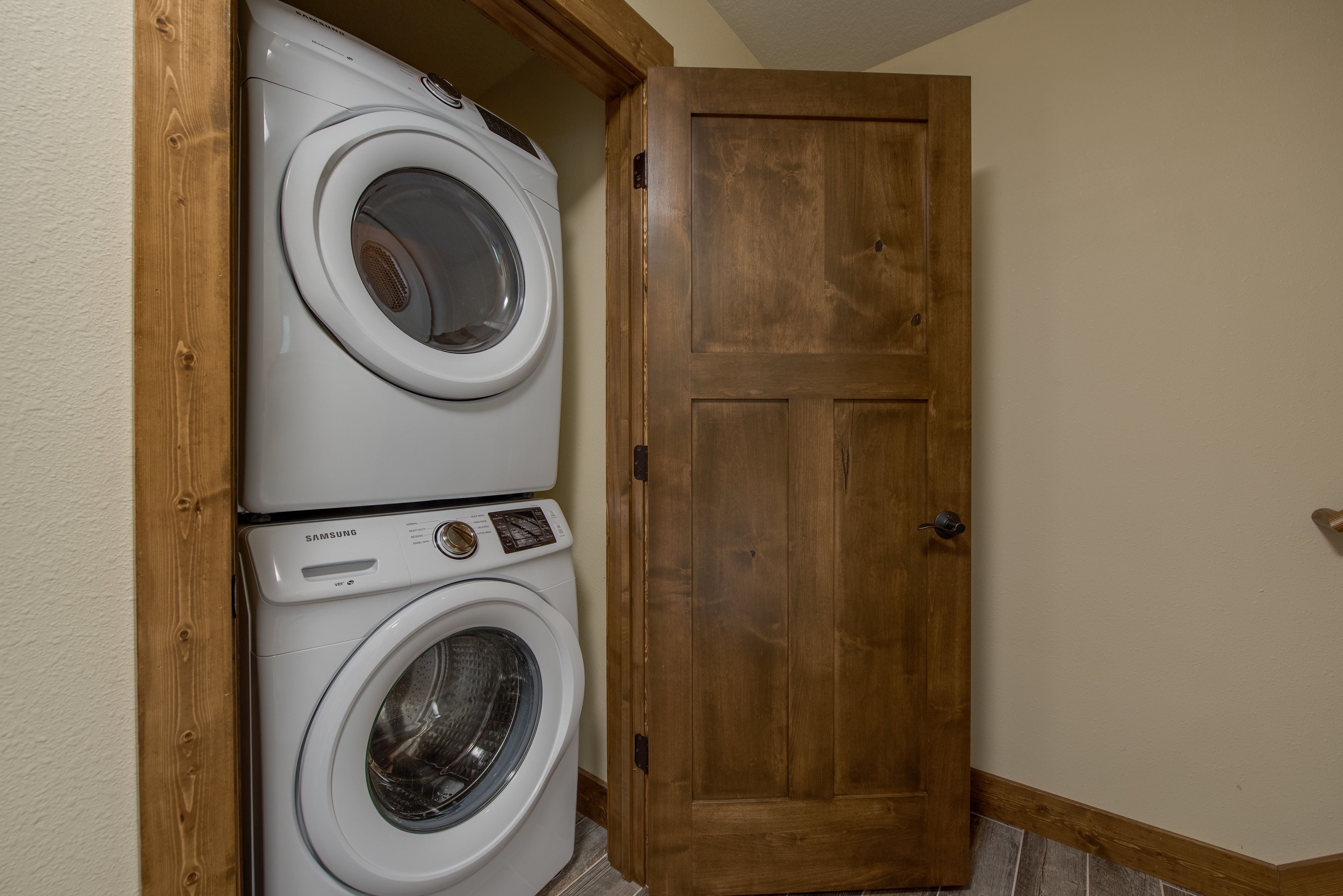 A laundry room with two stacked front-loading washing machines and a wooden door.