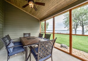 A covered patio with a wooden table and chairs, large windows overlooking a lake. - Lake Darling Resort (Alexandria)