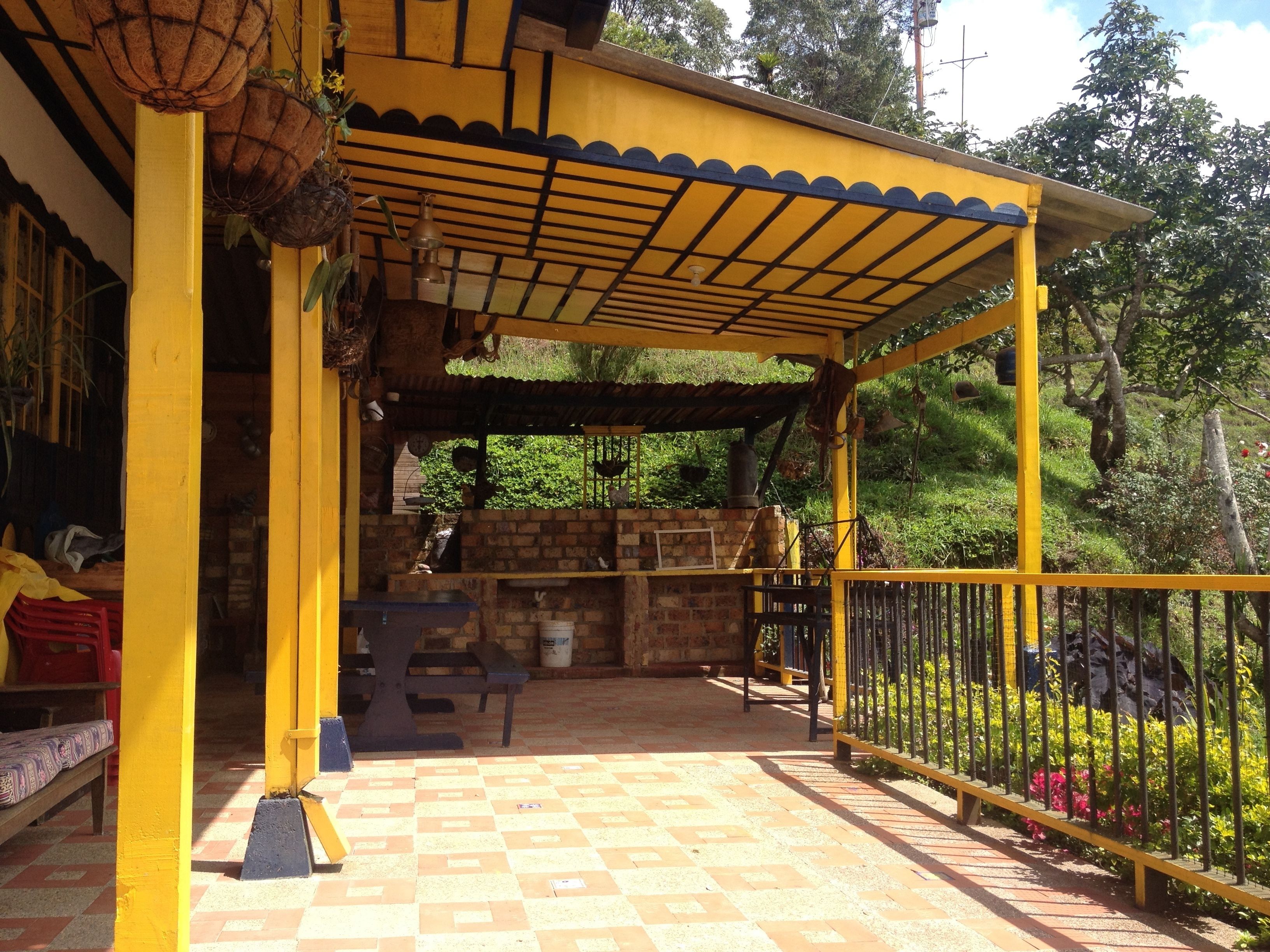 A covered outdoor seating area with a checkered floor, yellow railings, and a brick wall in the background.