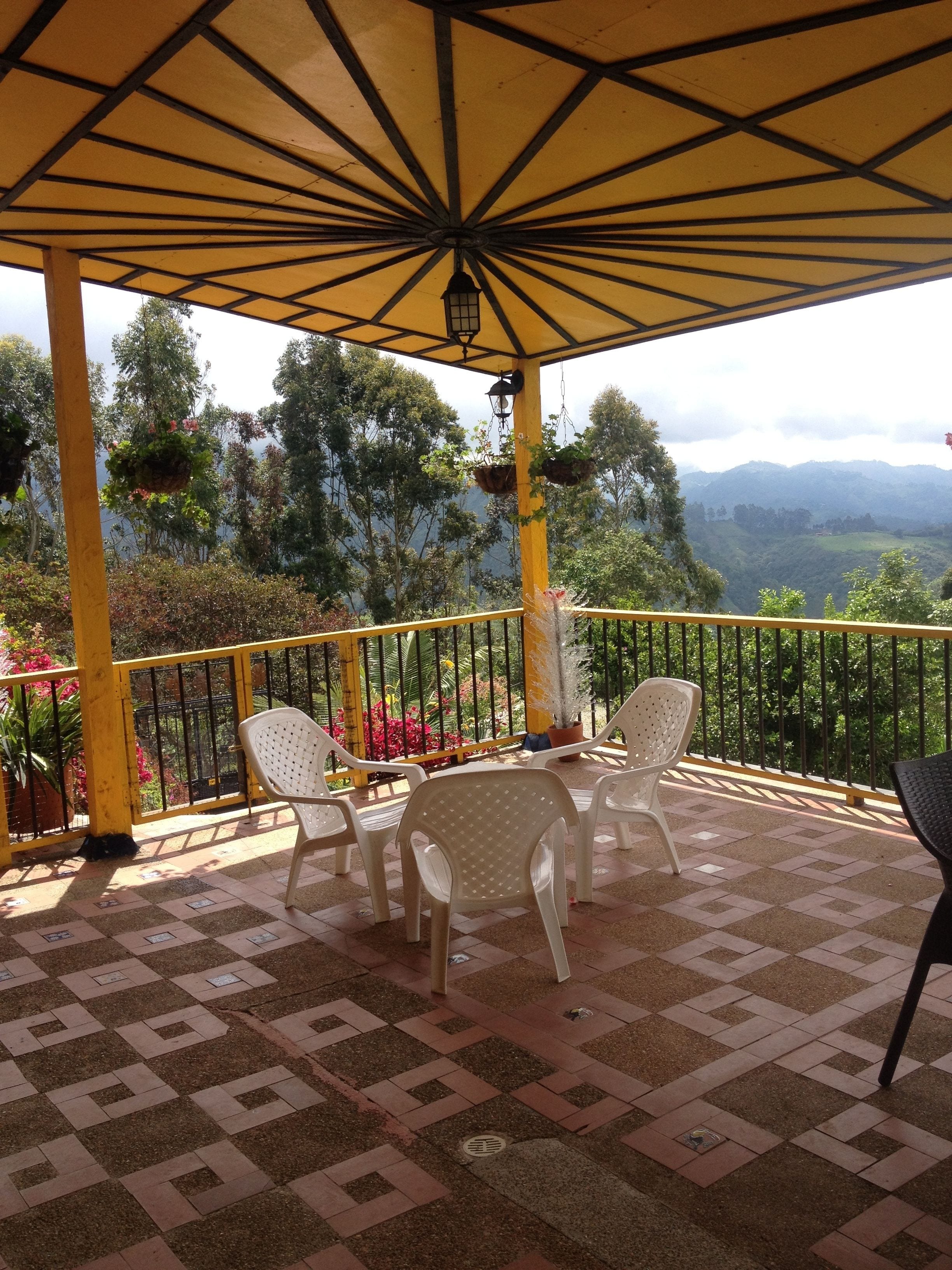Un patio techado con suelo de baldosas, sillas de plástico blanco y barandilla amarilla.