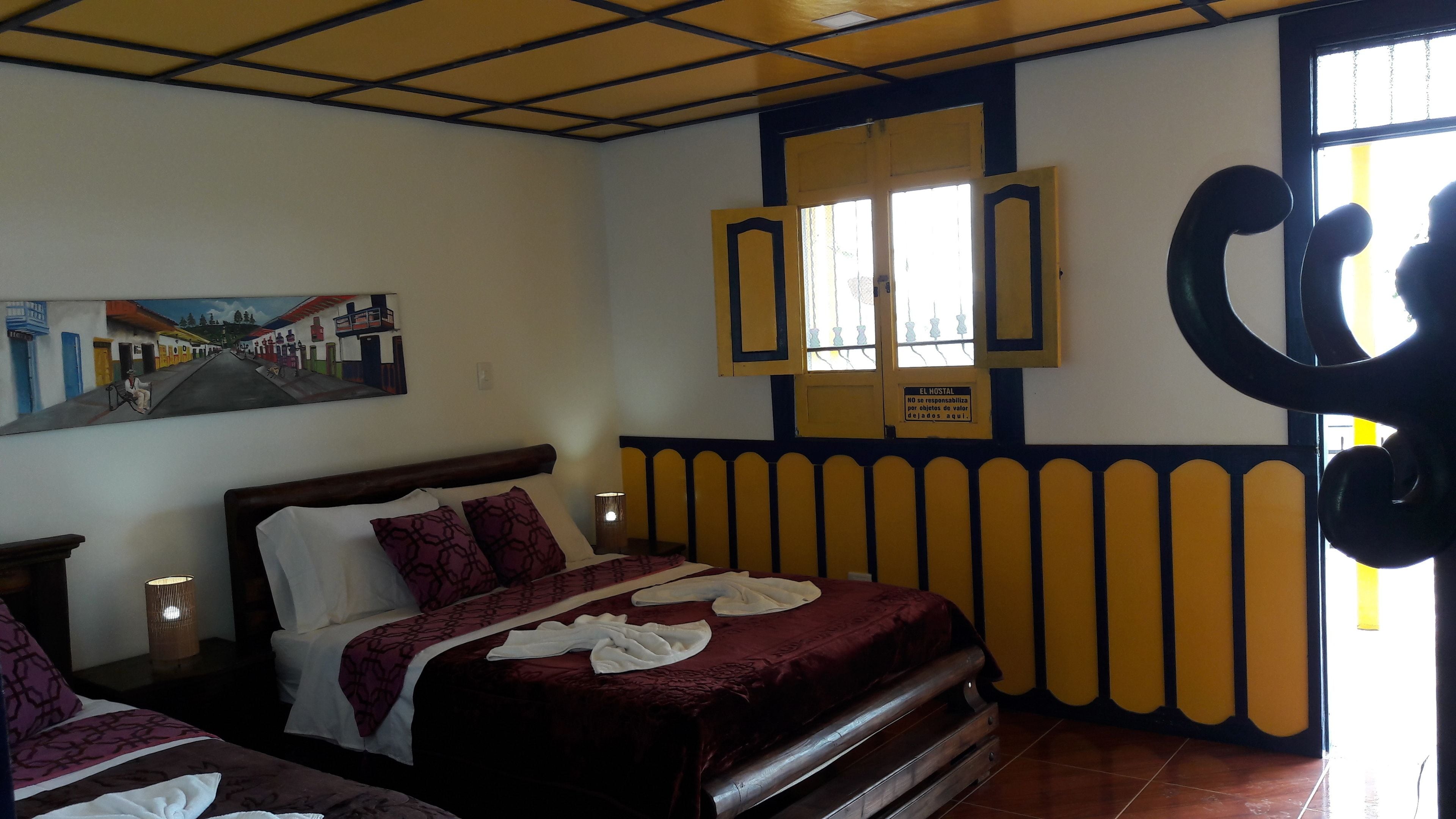 A hotel room with a bed, a nightstand, a lamp, a painting on the wall, and a window with a view.