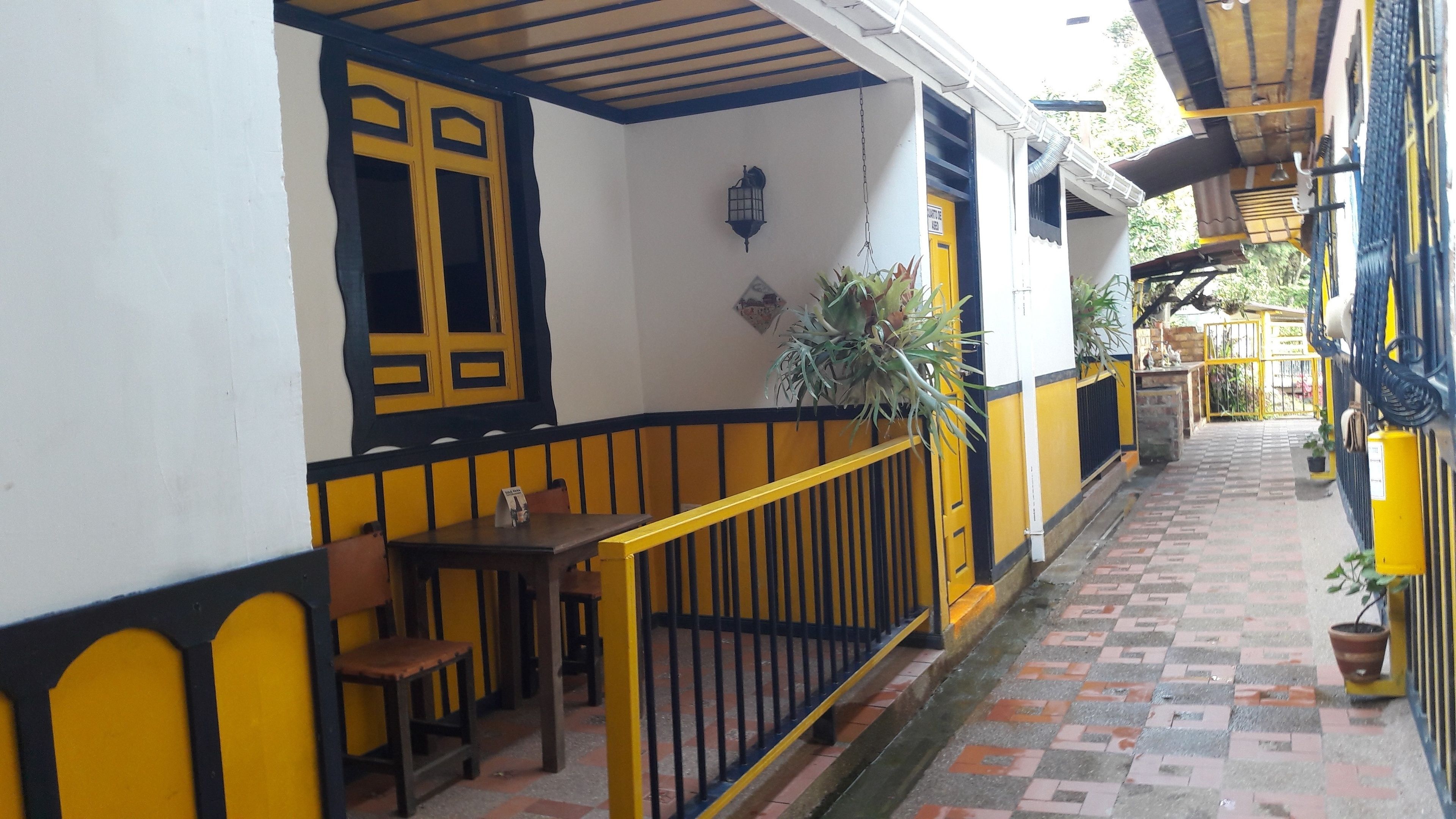 Un espacio exterior cubierto con barandillas amarillas y negras, una mesa con sillas y plantas en macetas.