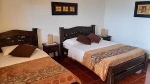 A hotel room with two single beds, each with a wooden headboard, a nightstand, and a lamp. The room has a tiled floor and plain walls. - Hostal Finca Cardonales (Salento)