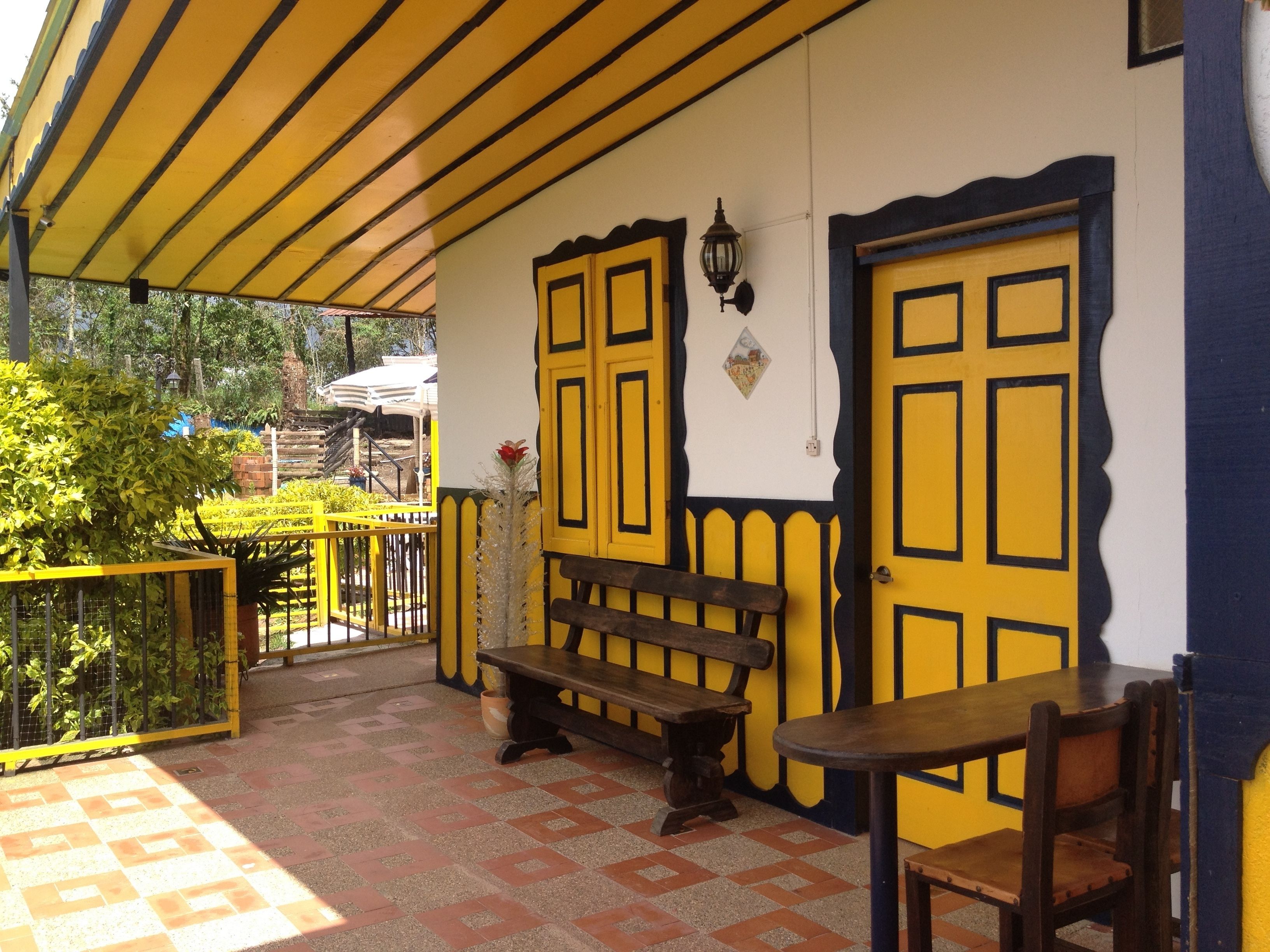 Un patio techado con paredes amarillas y azules, un banco de madera y una mesa.