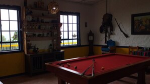 A pool table in a room with a window, shelves with various items, and a clock on the wall. - Hostal Finca Cardonales (Salento)
