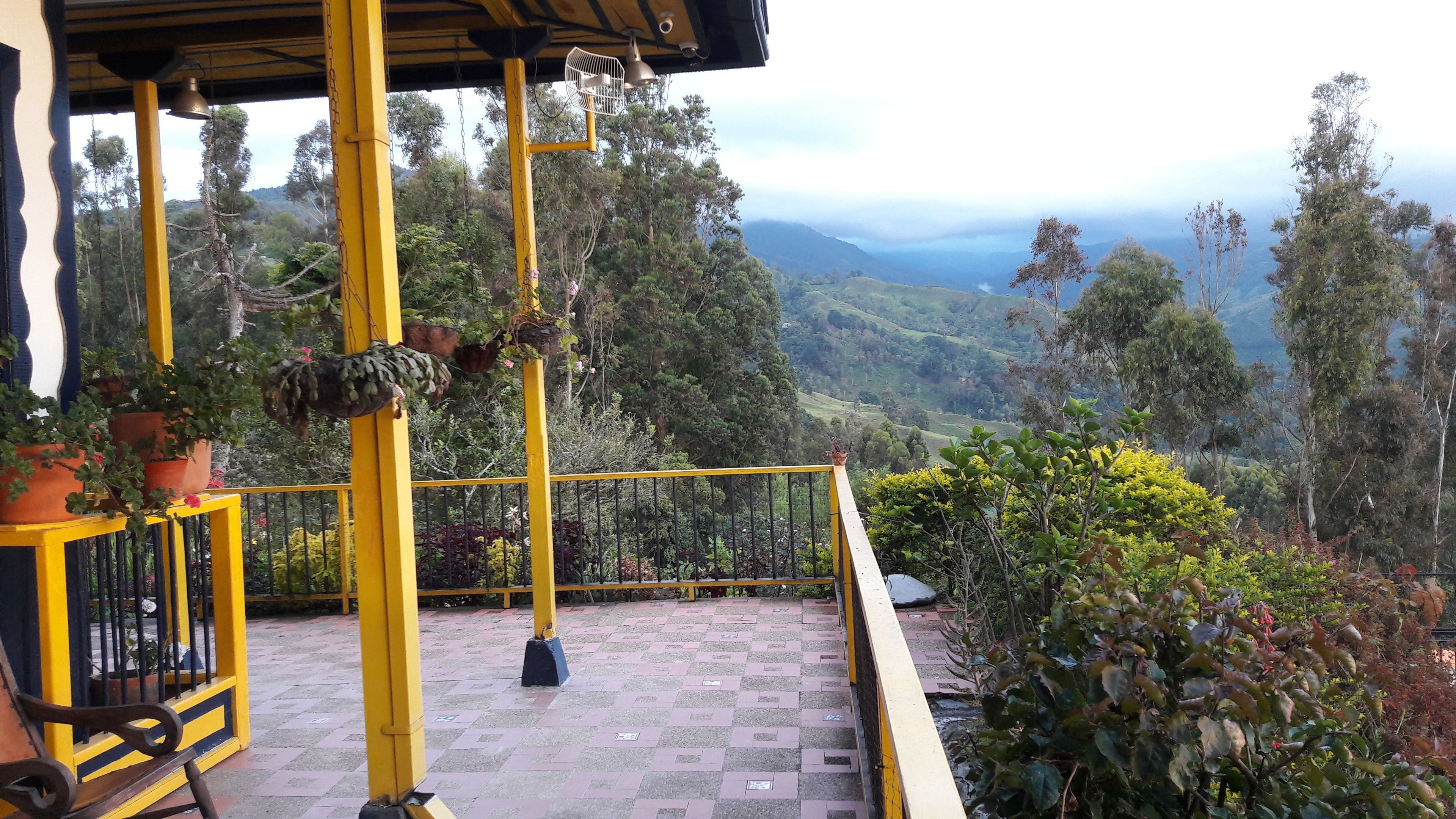 Una terraza con barandas amarillas, plantas en macetas y vistas a un paisaje montañoso.