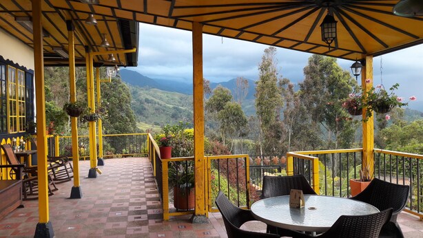 A covered outdoor seating area with yellow railings, a table, and chairs. - Hostal Finca Cardonales (Salento)