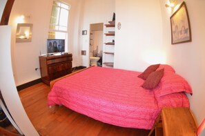 A bedroom with a large bed, wooden dresser, and a television on a stand.