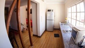 Una cocina con piso de madera, un refrigerador, un microondas y una ventana con persianas.