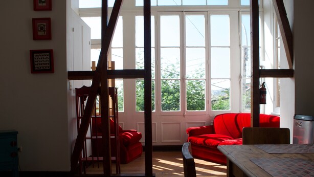 Una habitación con piso de madera, un sofá rojo, una mesa de madera y una ventana que da a vistas de vegetación.