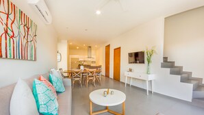 A modern living room with a sofa, coffee table, and dining area. There is a staircase and a TV mounted on the wall. - Amazing 2BR PH steps distance from 5th Av by Happy Address (Playa del Carmen)