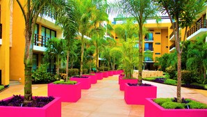 A hotel courtyard with a central pathway flanked by vibrant pink planters and lush greenery. - Amazing 2BR PH steps distance from 5th Av by Happy Address (Playa del Carmen)