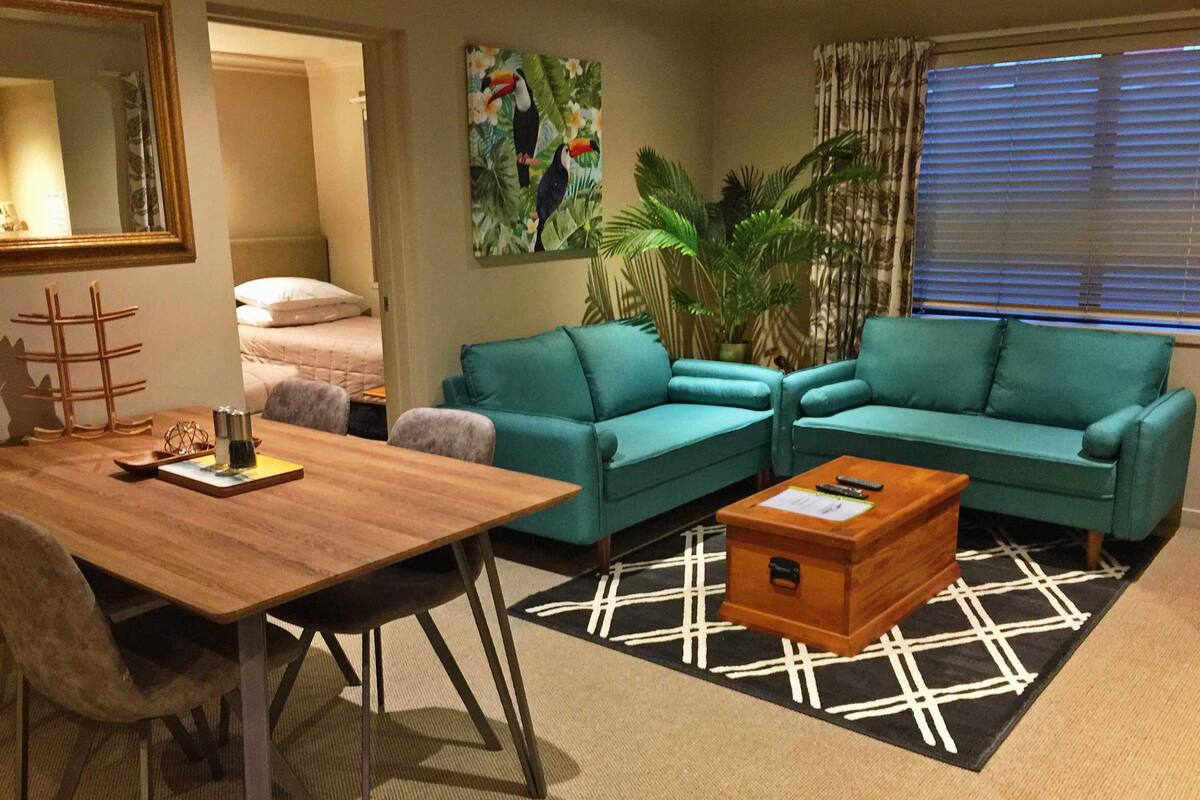 A living room with teal sofas, a wooden coffee table, a black and white rug, and a painting of toucans.