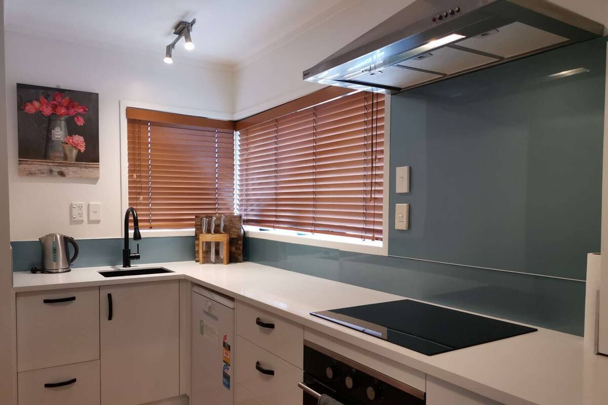 A modern kitchen with white cabinets, a black stove, and a window with blinds.