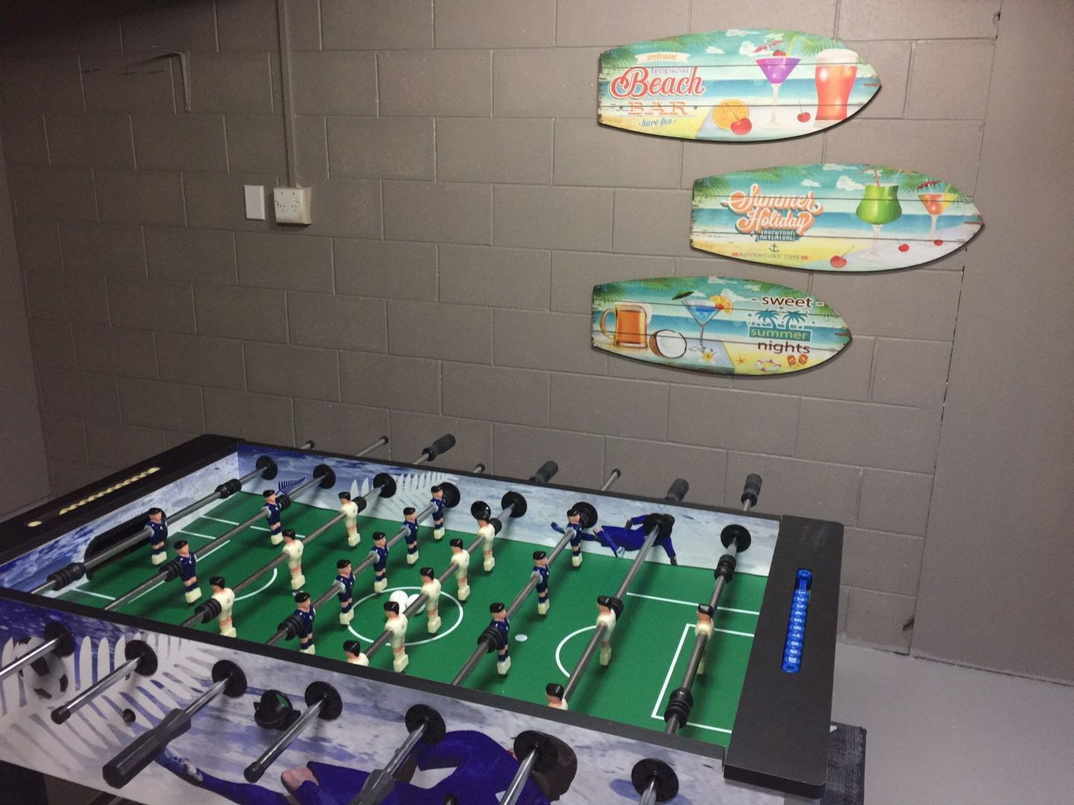 A foosball table with a soccer field layout, surrounded by a brick wall with three decorative signs.