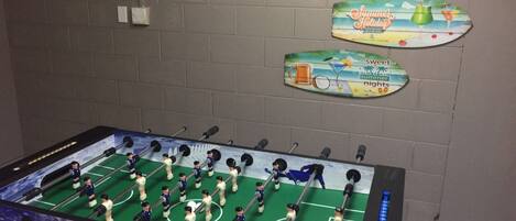 A foosball table with a soccer field layout, surrounded by a brick wall with three decorative signs.