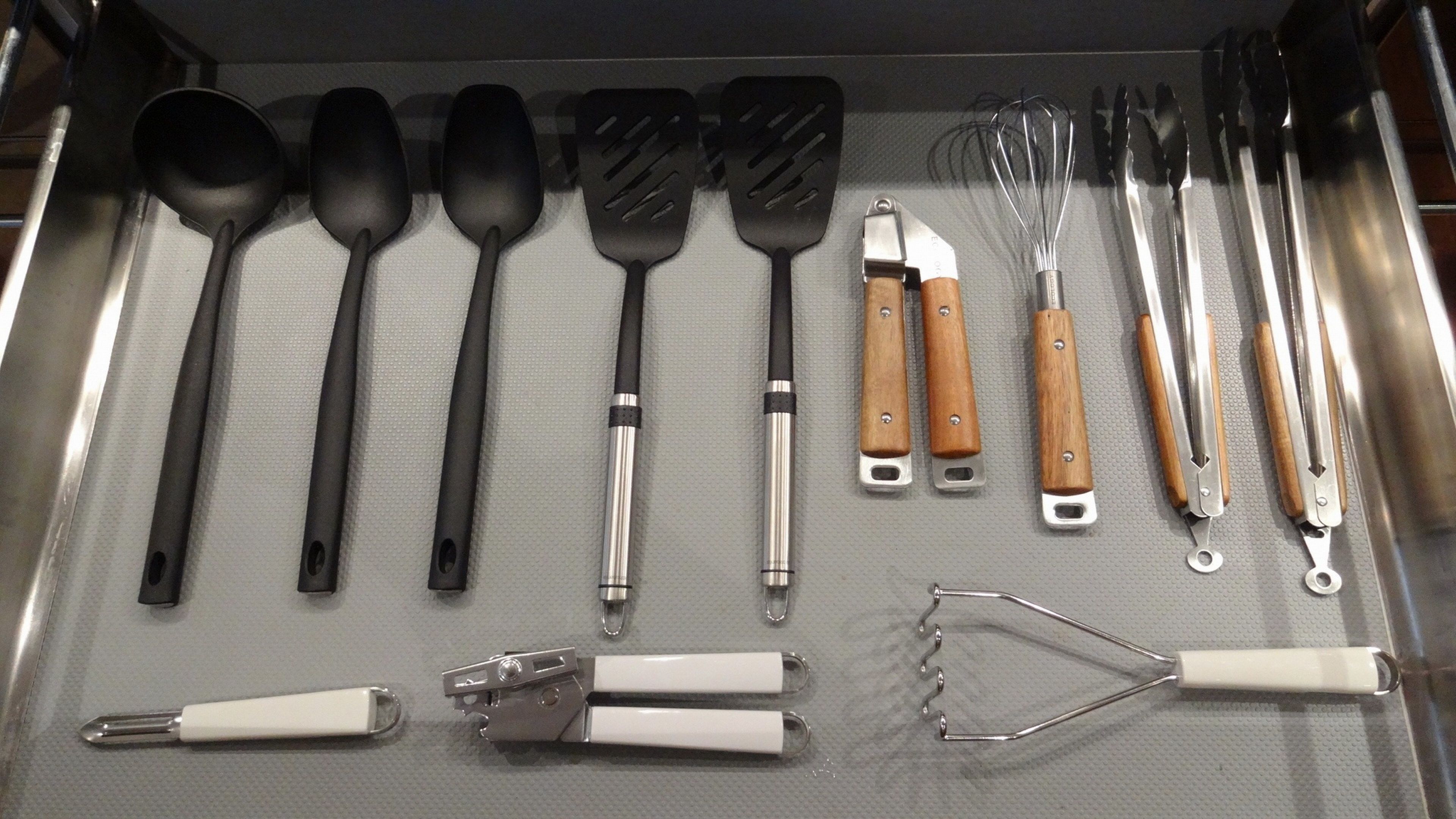Un cassetto pieno di utensili da cucina, come cucchiai, spatole, fruste, pinze e una grattugia.