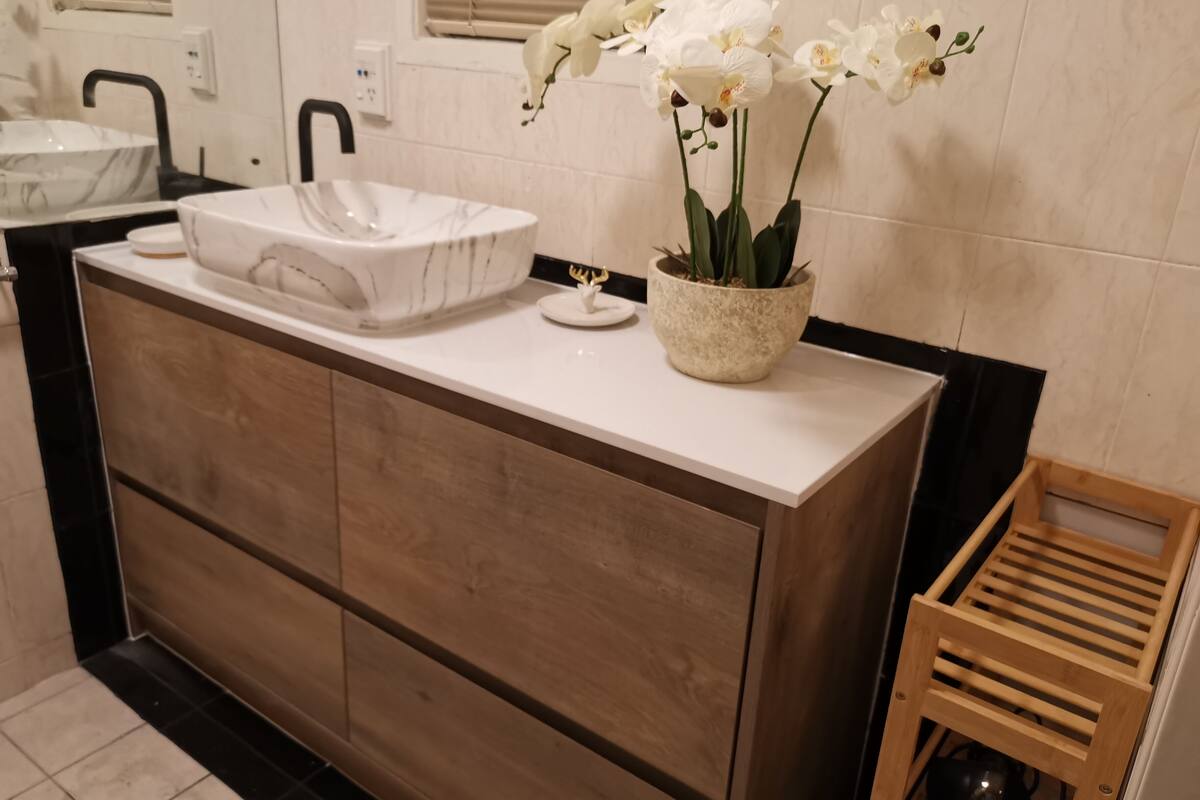 A modern bathroom with a marble sink, wooden cabinetry, and a potted orchid.