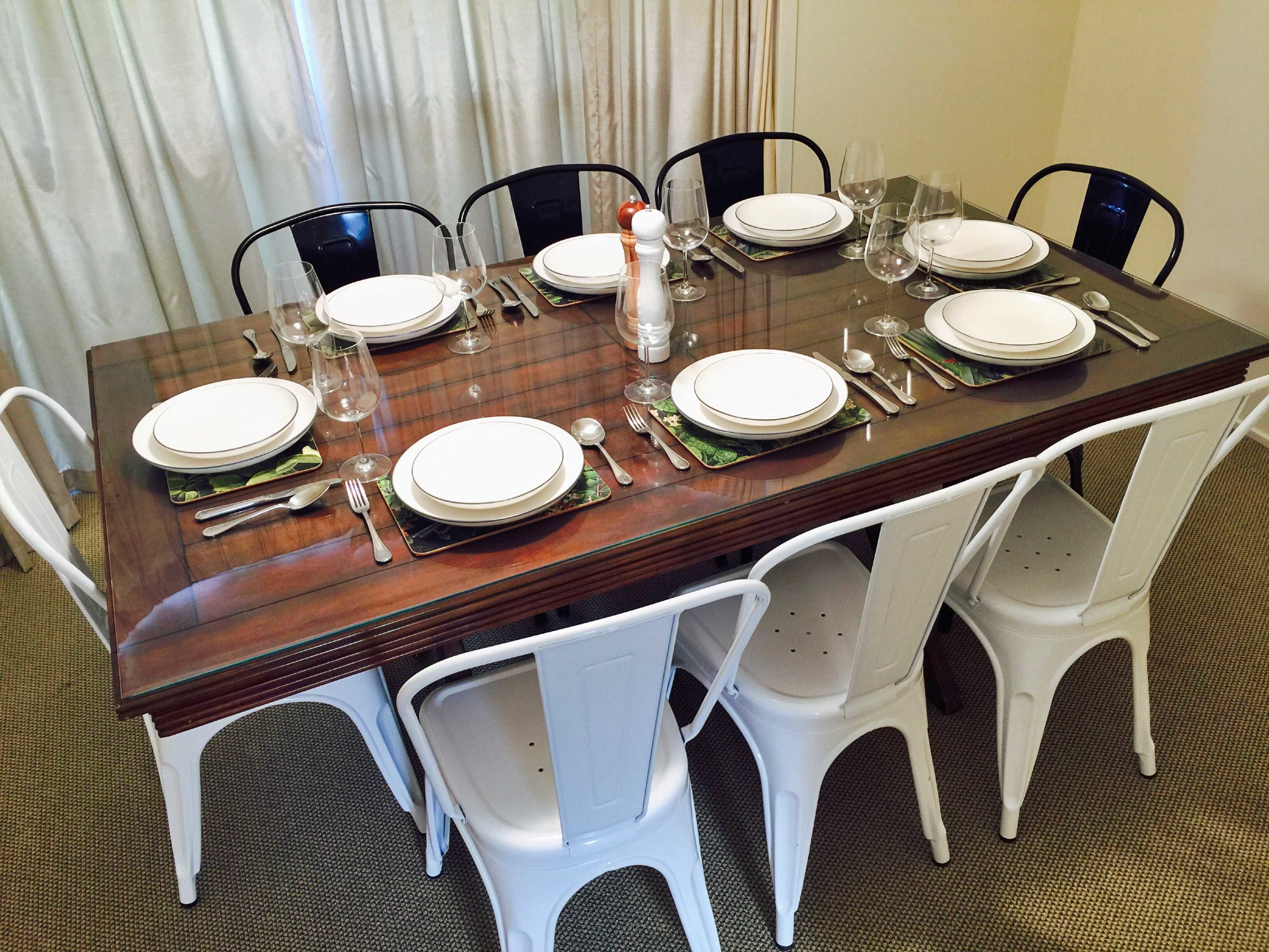 Mesa para seis personas con sillas blancas, superficie de vidrio y un centro de mesa decorativo.