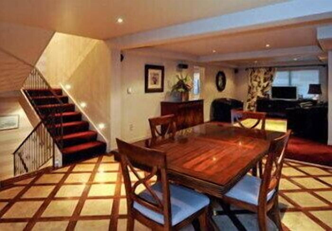 A dining area with a wooden table and chairs, a staircase, and a living area with a sofa and a TV.