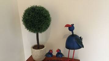 Un letrero de bienvenida, un árbol en maceta y dos esculturas de aves sobre una mesa de madera.