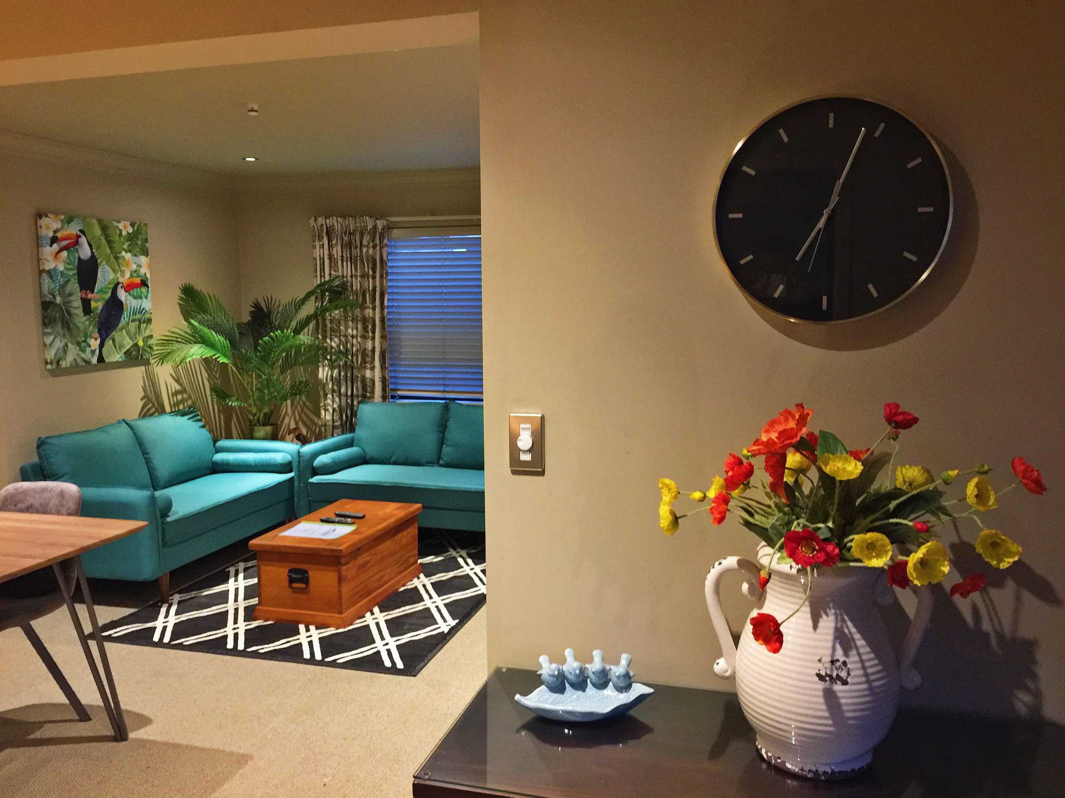 A living room with teal sofas, a wooden coffee table, a clock, and a vase with flowers.