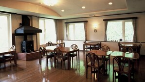 A dining area with wooden tables and chairs, a brick fireplace, and large windows with curtains. - Guesthouse Hilltop (Kiso)
