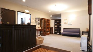 A room with a wooden bench, a sofa, a cabinet with glass doors, and a refrigerator. - Guesthouse Hilltop (Kiso)