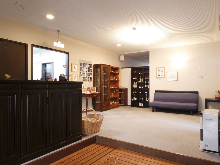A room with a wooden bench, a sofa, a cabinet with glass doors, and a refrigerator.