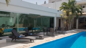 A modern pool area with lounge chairs, a glass-enclosed dining area, and palm trees. - Nonna Mia (Campeche)