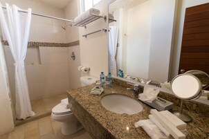Un baño con lavamanos de granito, un inodoro, ducha con puerta de vidrio y un espejo con marco redondo.