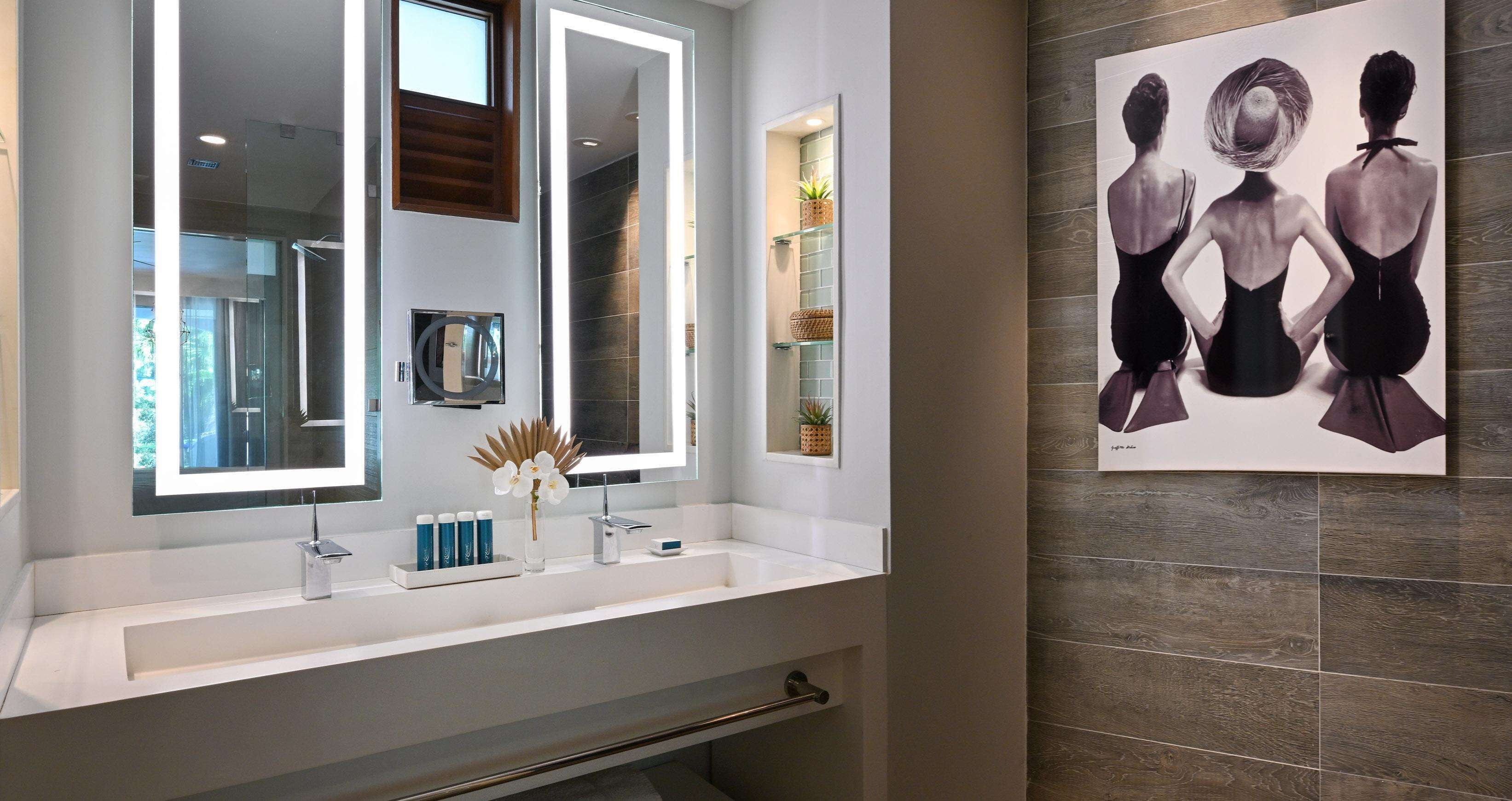 Een moderne badkamer met een grote spiegel, een witte wastafel en een decoratieve vaas.