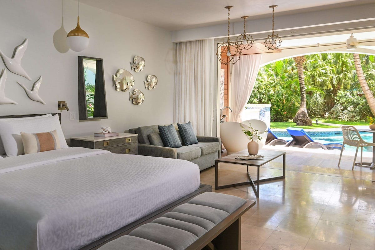 A spacious bedroom with a large bed, a sofa, and a view of a swimming pool.