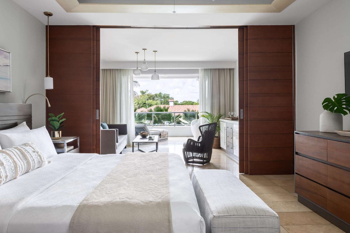 A modern hotel room with a large bed, a seating area with a view, and a TV on the wall.