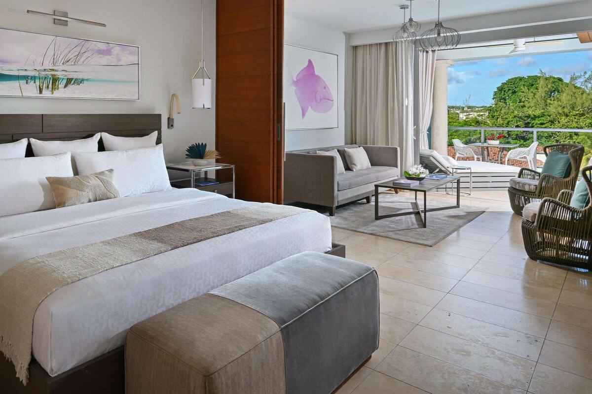 A modern hotel room with a large bed, a balcony with outdoor seating, and artwork on the walls.