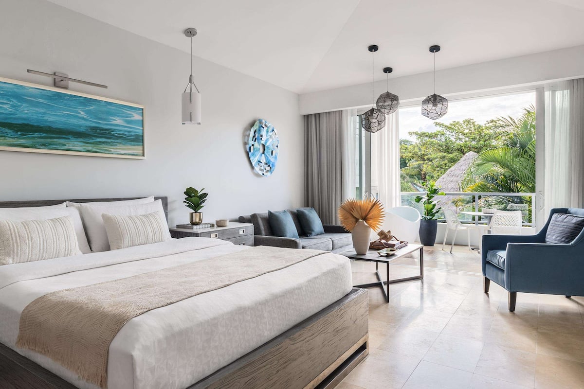 A modern bedroom with a large bed, a sofa, a coffee table, and a view of the outdoors.