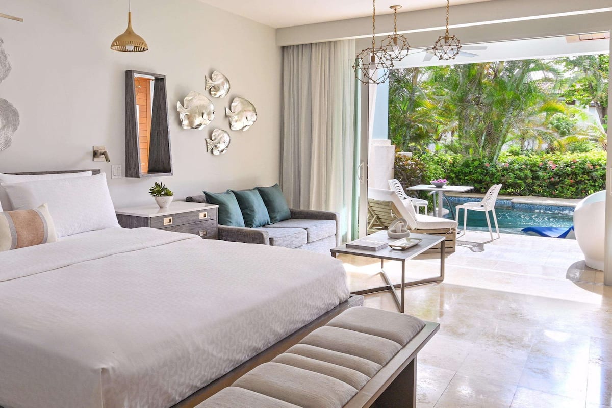 A modern hotel room with a large bed, a seating area with a view of the pool, and decorative wall art.