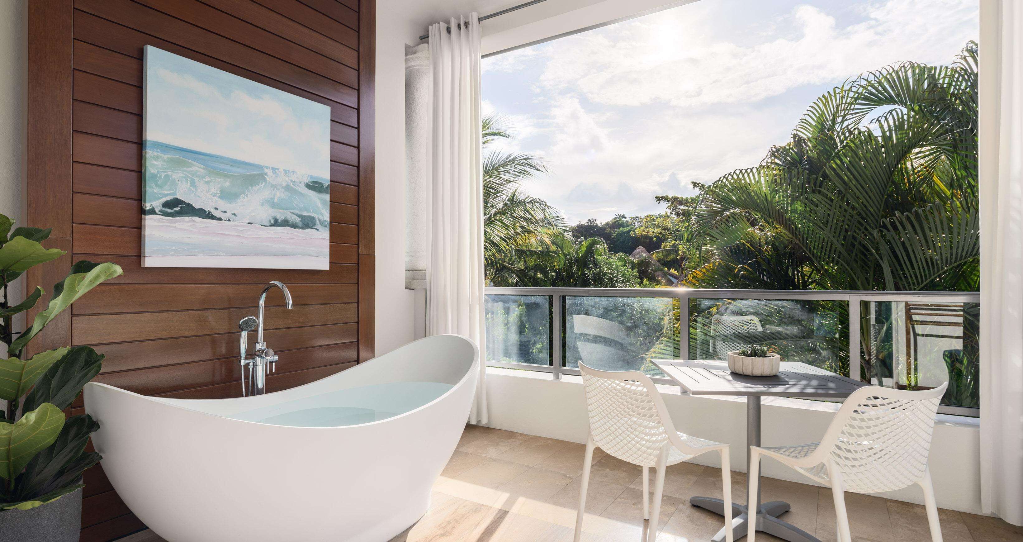 A modern bathroom with a freestanding bathtub, a wooden panel wall, and a large window overlooking a tropical garden.