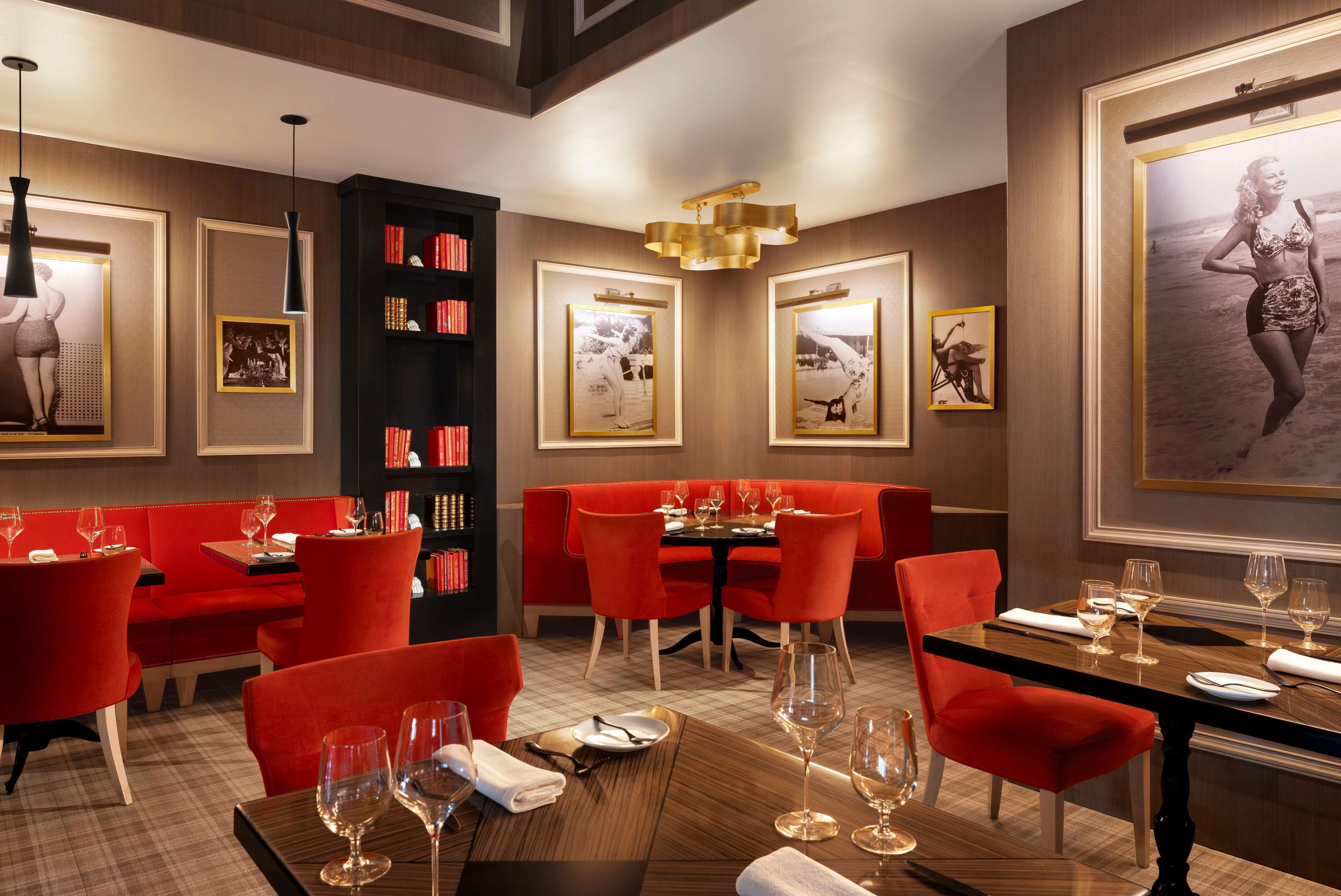 Un restaurant avec des sièges rouges, une bibliothèque noire, des tableaux encadrés accrochés au mur et un grand tableau encadré sur le côté droit.
