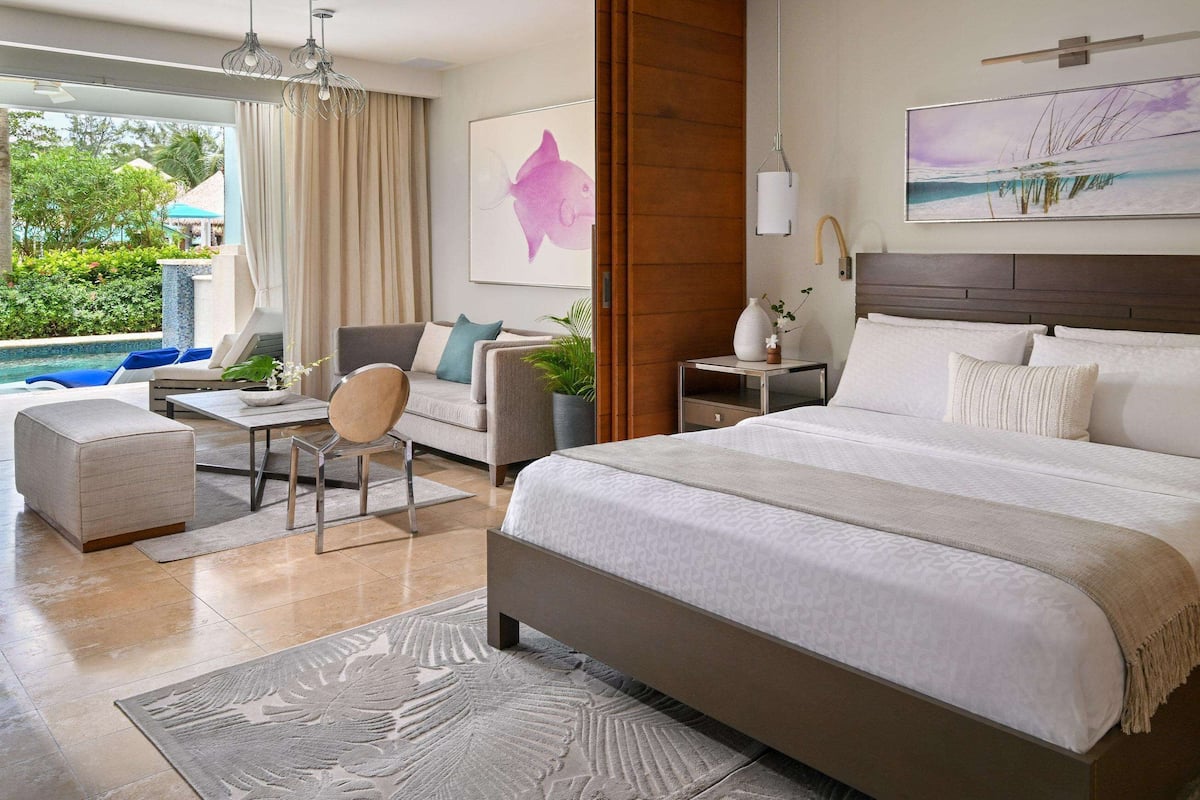 A modern hotel room with a large bed, a desk, and a view of a swimming pool.