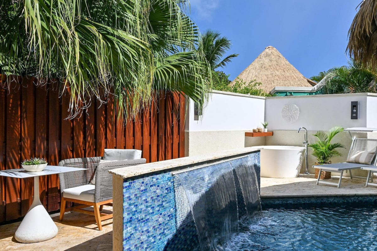 A pool area with lounge chairs, a hot tub, and a waterfall feature.