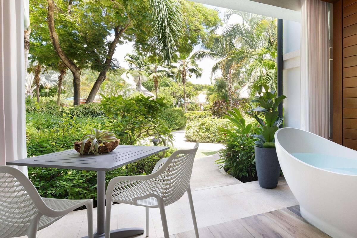 A bathroom with a freestanding bathtub, a table with chairs, and a view of a lush garden.