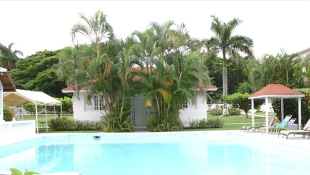 A swimming pool with lounge chairs and a gazebo, surrounded by palm trees and a small building. - Executive Mamme Bay Hotel and Conference (Ocho Rios)