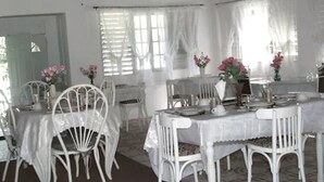 A dining area with white tables and chairs, covered with white tablecloths, and adorned with pink flowers in vases. - Executive Mamme Bay Hotel and Conference (Ocho Rios)
