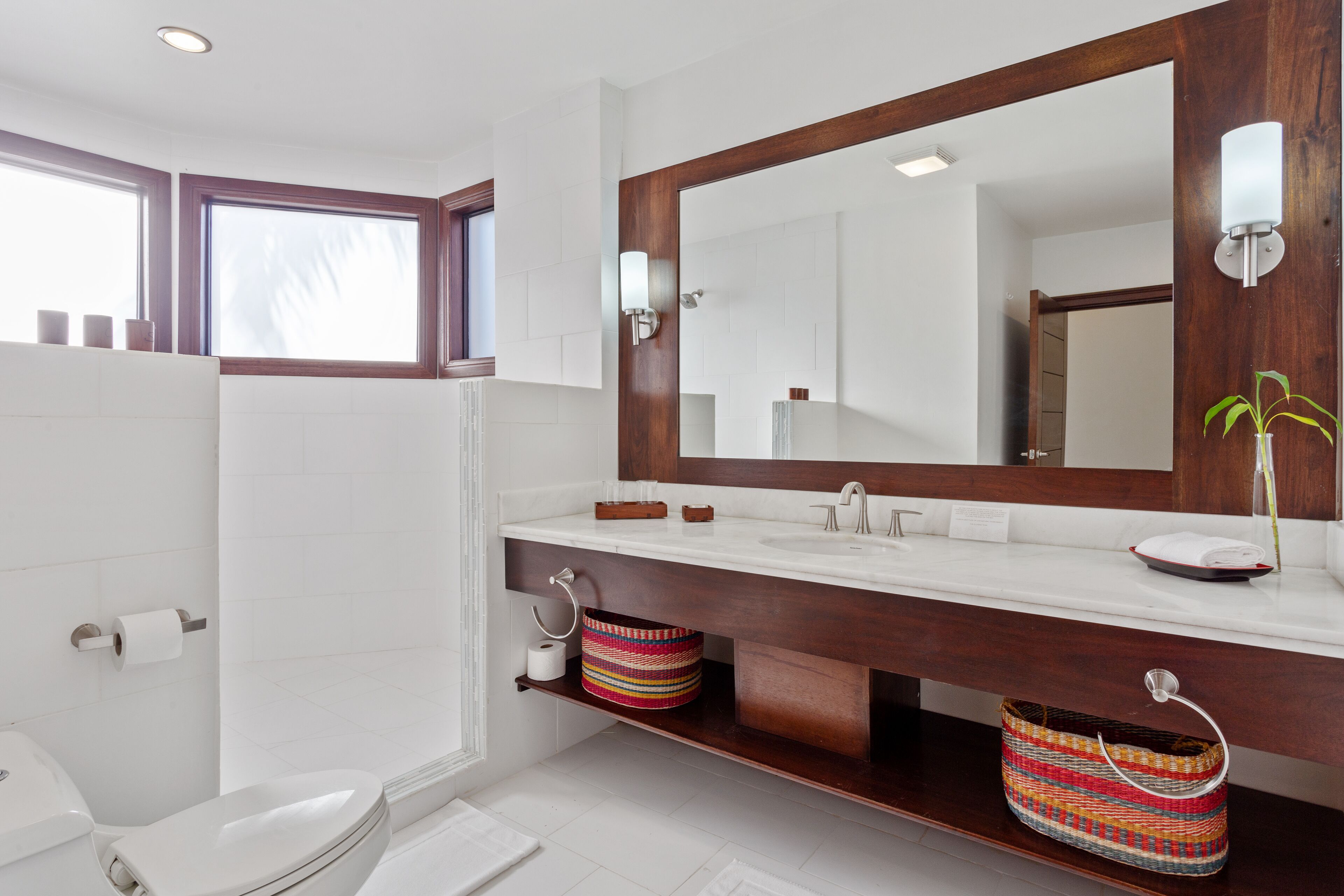 A modern bathroom with a large mirror, white tiles, a wooden vanity, and a shower area.